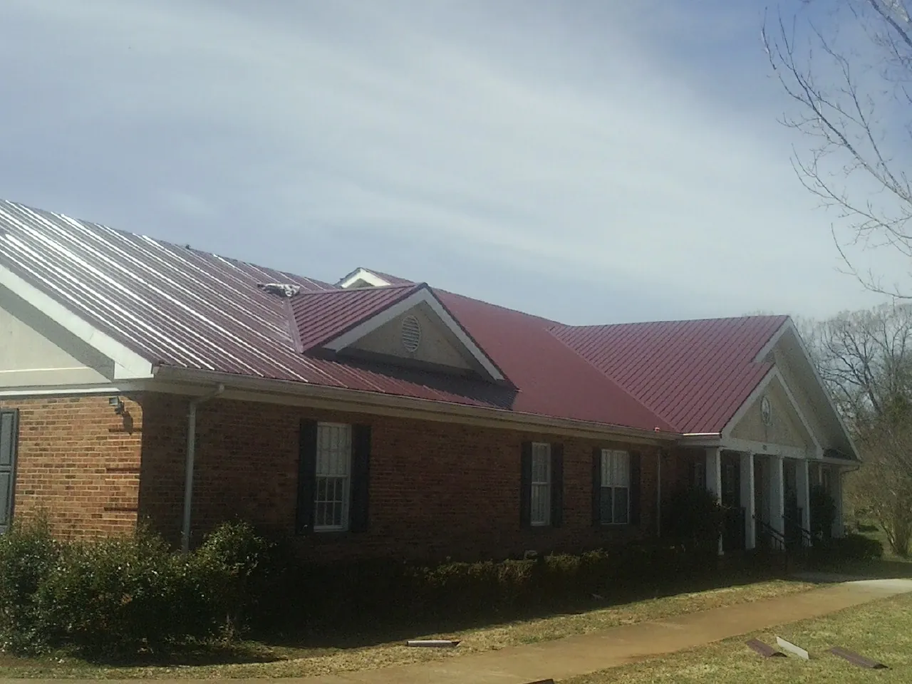 Red metal roof with gabled entries on a long brick building, from a Hail Damage Roof Repair job in Rockvale
