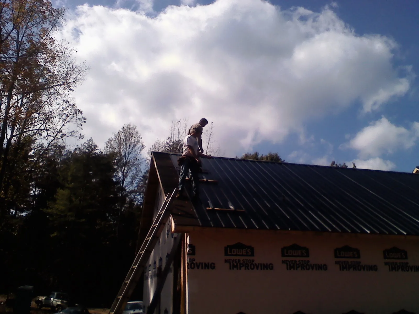 Roofer fastening dark metal panels high against a cloudy sky in Rockvale